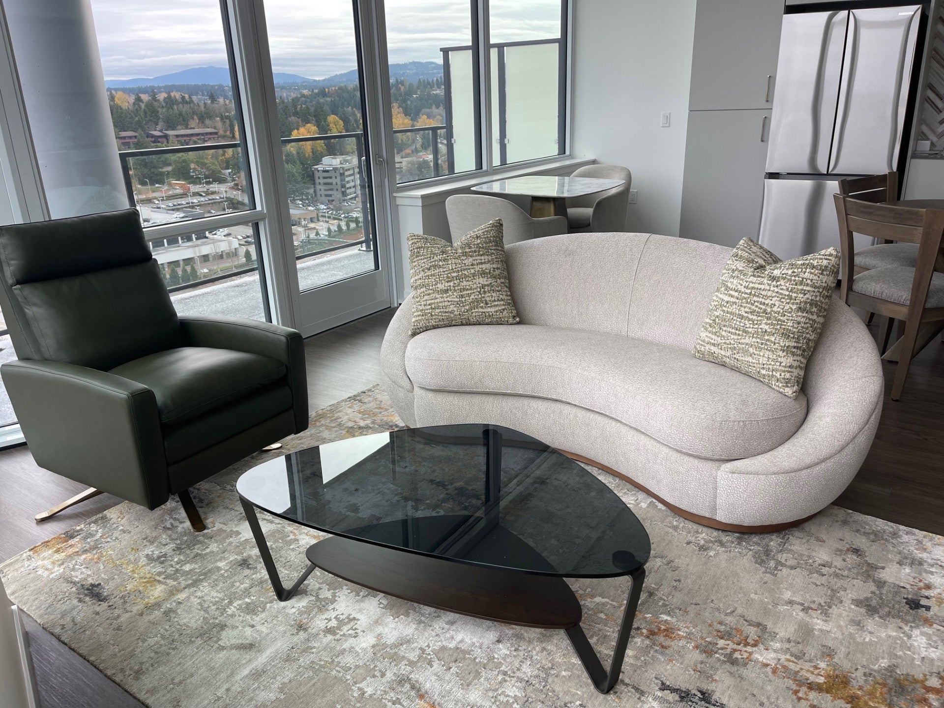 Modern living room with a curved gray sofa, black armchair, and glass coffee table and wool & Silk modern area rug.